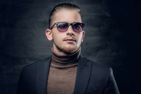 Portrait of blonde, stylish male in sunglasses in turtle-neck sweater on dark grey background.の写真素材