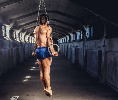 Full body portrait of athletic gymnast exercising on stationary rings in a tunnel.の写真素材