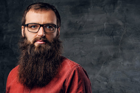 Portrait of a bearded hipster male in eyeglasses dressed in a red shirt on grey background.の写真素材