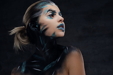 Portrait of a woman with artistic make up on a face and neck isolated on dark grey background.