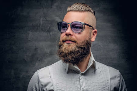 Studio portrait of bearded male with punk hairstyle dresses in a white shirt and violet sunglasses on grey vignette background.の写真素材