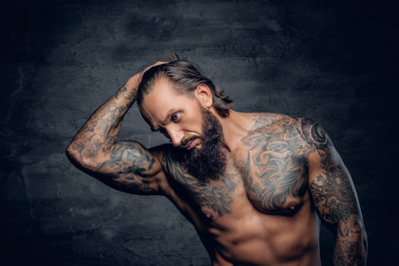 Muscular bearded male with tattooed body isolated with illumination on grey background.の写真素材