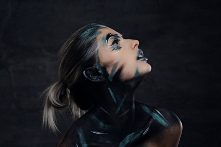 Side view close up portrait of a woman with artistic make up looking up on dark background.