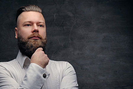 Thoughtful bearded male in a white shirt on grey background.の写真素材