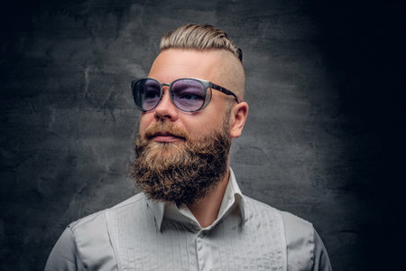 Studio portrait of bearded male with punk hairstyle dresses in a white shirt and violet sunglasses...