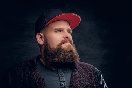 Brutal bearded male in baseball hip hop cap isolated on grey vignette background.