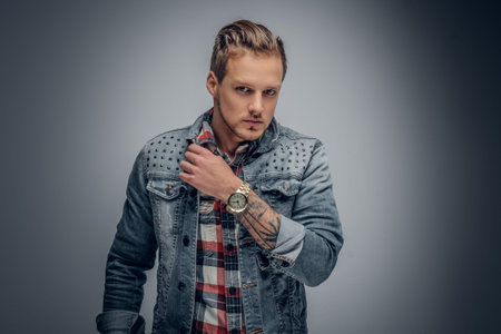 Positive blond bearded male dressed in a plaid shirt and denim jacket posing in the grey vignette background.の写真素材
