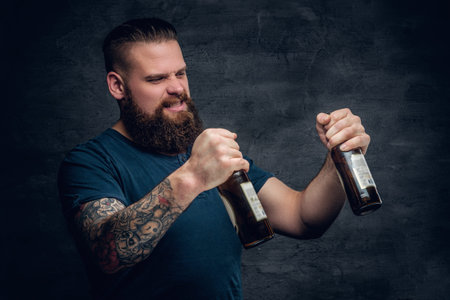 Alcohol addiction. Bearded male looking at two empty beer bottles.
