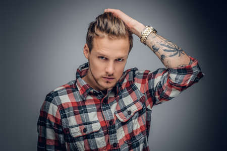 Portrait of a blond male with tattooed arm on his head dressed in a plaid shirt isolated on grey vignette background.の写真素材