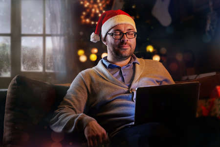 A man in Santa's hat holds laptop and dreaming about gifts on Christmas.の写真素材