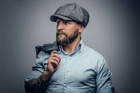 Middle age bearded male with tattooed arms, dressed in a white shirt and a tweed cap.の写真素材