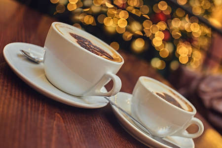 Two white cups with aroma refreshing coffee on a table with illumination lights on the background.の写真素材