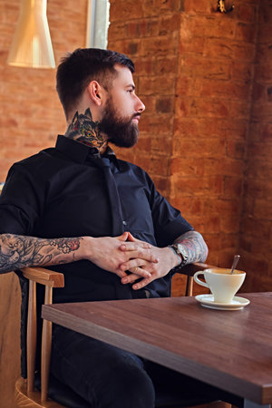 Bearded hipster male with tattooed arms resting at the table with cup of coffee.の写真素材