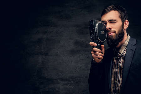 A stylish bearded male dressed in a suit holds vintage 8mm video camera.の写真素材