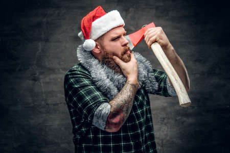 Studio portrait of bearded male in Santa's hat holds the axe.の写真素材