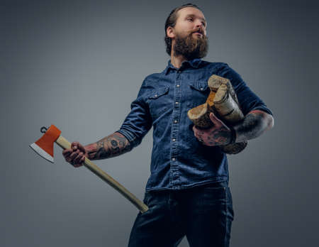 Bearded male with tattoos on his arms holds an axe and firewoods.の写真素材