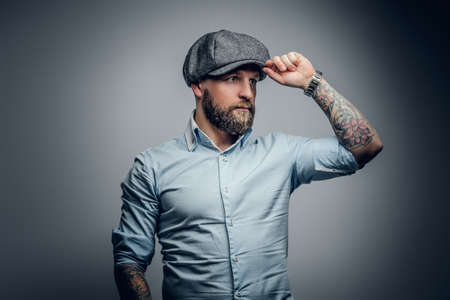 Middle age bearded male with tattooed arms, dressed in a white shirt and a tweed cap.の写真素材
