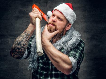 Studio portrait of bearded male in Santa's hat holds the axe.の写真素材