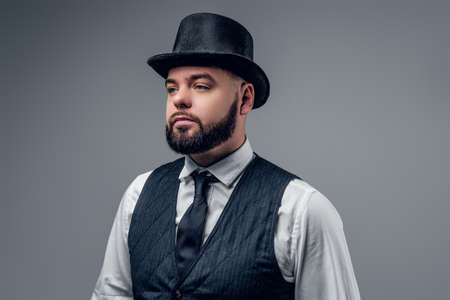 Portrait of elegant bearded male dressed in a waistcoat and a cylinder hat isolated on grey background.の写真素材