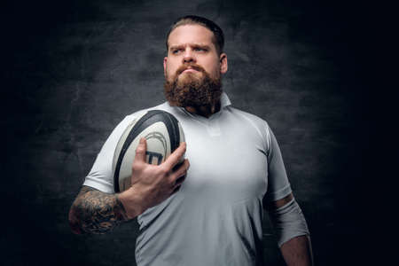 Portrait of bearded rugby player with tattoos on his arms holds a game ball.の写真素材