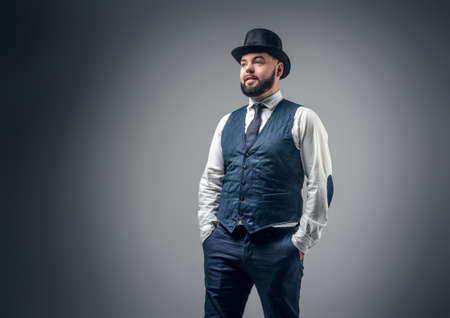Portrait of elegant bearded male dressed in a waistcoat and a cylinder hat in grey vignette background.の写真素材