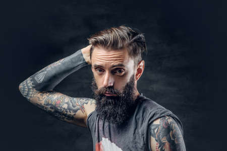 Portrait of a tattooed, bearded male in a t shirt touches his head over a dark background.の写真素材