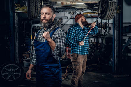 Two brutal bearded mechanics repairing a car in a garage.の写真素材