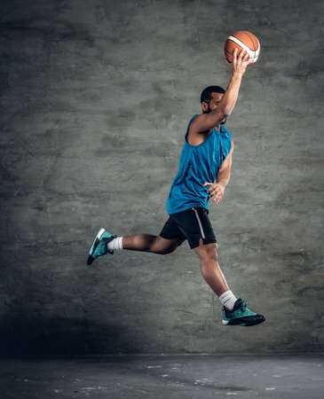 Jumping black man basketball player in a blue sportswear over grey background.の写真素材