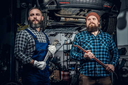 Two brutal bearded mechanics repairing a car in a garage.の写真素材