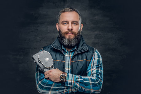 Portrait of bearded middle age male holds vintage 8 mm video camera over grey background.の写真素材