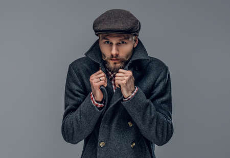 Portrait of a bearded man dressed in a worm jacket and wool cap isolated on grey background.の写真素材