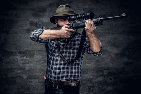 Studio portrait of bearded hunter male wearing a plaid fleece shirt holds a rifle.の写真素材