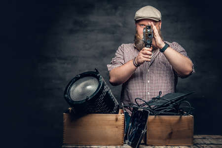The fat bearded hipster male holds vintage 8 mm video camera and colorful soffits lamps.