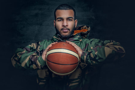 A black male in a camouflage hoodie holds basket ball.
