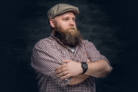 Portrait of fat bearded male in a cap over grey background.