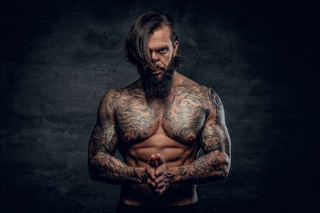 Studio portrait of bearded man with shirtless, tattooed body on grey background.の写真素材