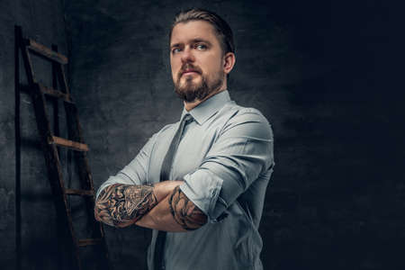 Stylish bearded male with tattooed arms, dressed in a shirt posing over grey background.の写真素材