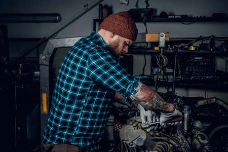 A brutal bearded man with tattooed arm repairing the car's engine in a garage.の写真素材
