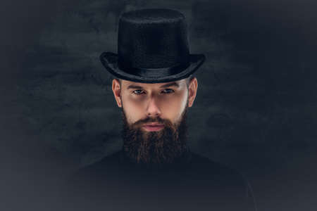Portrait of bearded hipster male dressed in a black shirt and a cylinder hat.の写真素材