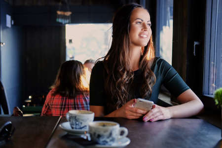 Smiling brunette woman using a smartphone in a cafe.の写真素材