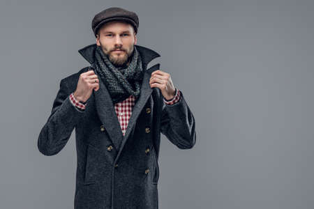 Portrait of a bearded hipster man dressed in a gray jacket and a wool cap isolated on grey background.の写真素材