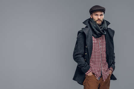 Portrait of a bearded hipster man dressed in a gray jacket and a wool cap isolated on grey...