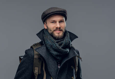 A stylish bearded hipster man dressed in a grey jacket holds a backpack.の写真素材