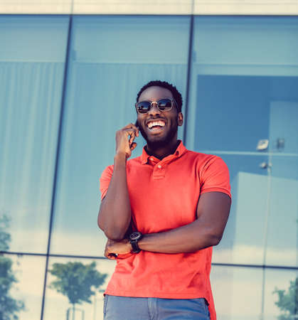 A positive Black male dressed in a red polo shirt posing on a street in a downtown.の写真素材