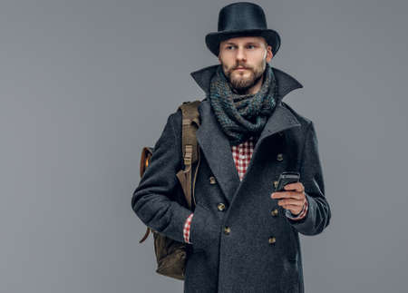 Portrait of bearded male dressed in a grey jacket and a hat isolated on grey background.の写真素材