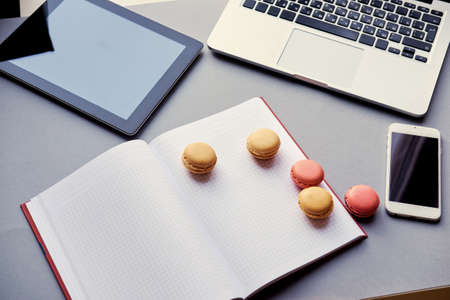 Open laptop, smart phone and tablet PC and small cakes on a table.