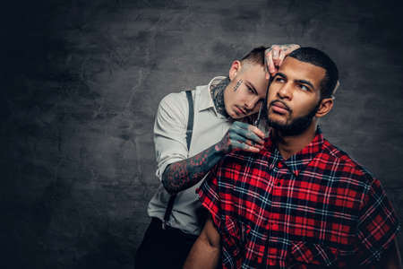 Tattooed barber cuts the beard to a Black bearded male.の写真素材