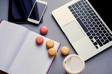 Open laptop, smart phone and tablet PC and small cakes on a table.の写真素材