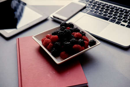 Open laptop, smart phone and tablet PC and a cup with berries on a table.