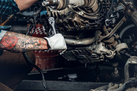 A man with tattoo on arm repairing engine of a car in a garage.の写真素材